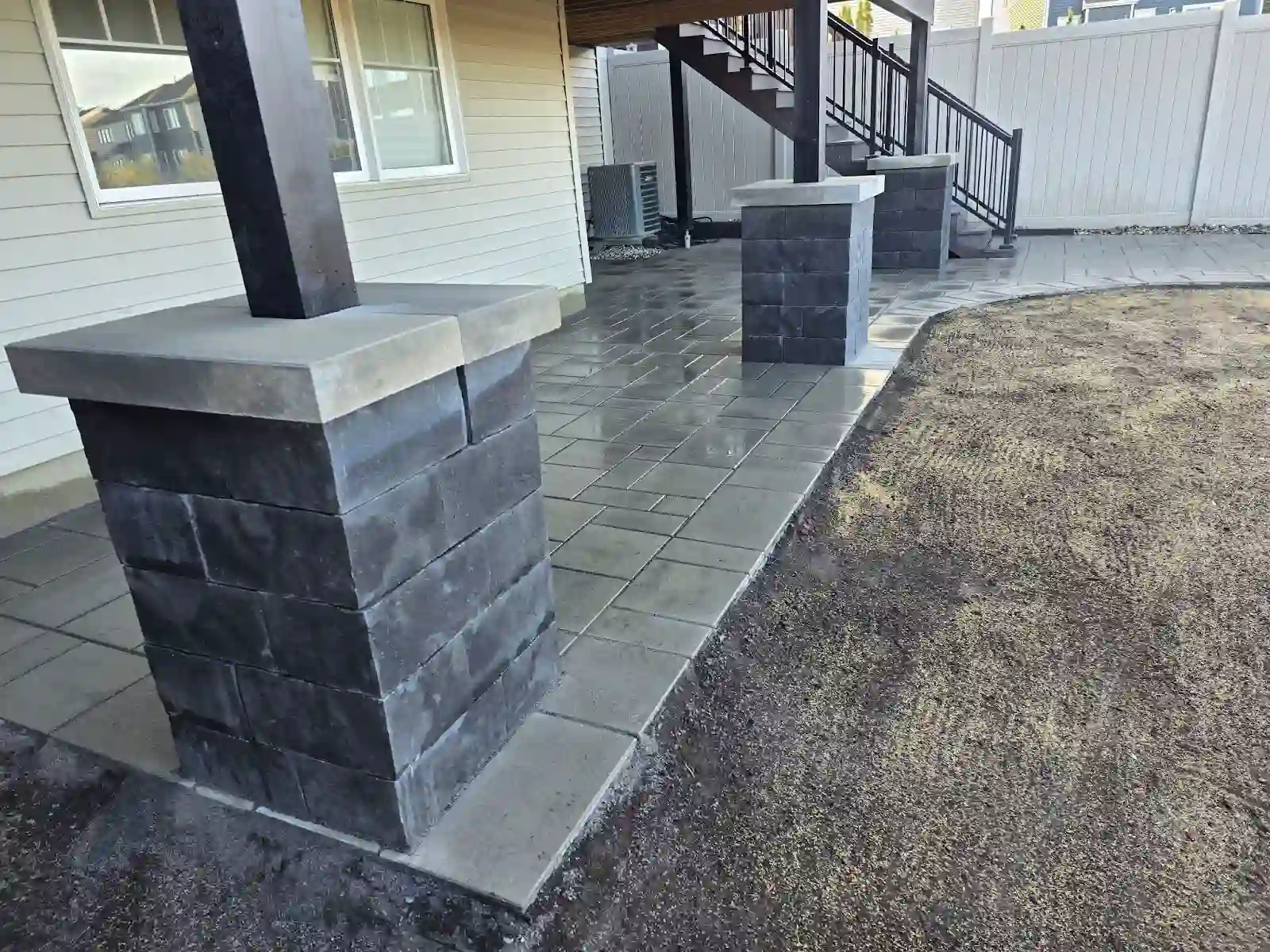 Grey interlock patio with charcoal stone pillars under a deck